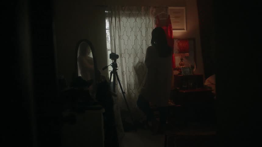 A person is standing in a room near a camera looking towards a window