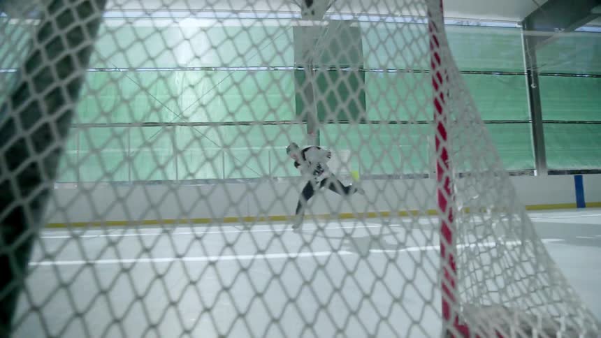 A hockey player is taking a shot at an empty hockey net inside during the day