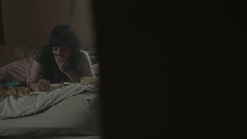 A woman lays in bed while writing in a notebook