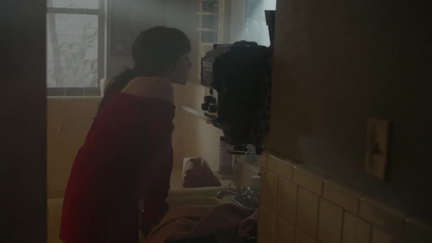 A woman leans on the sink and stares into the mirror