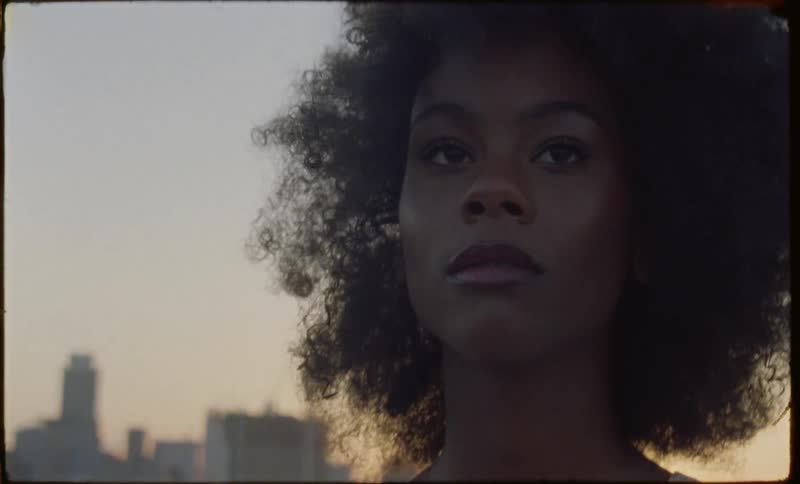 A black woman is standing on a rooftop and her hair is blowing in the wind