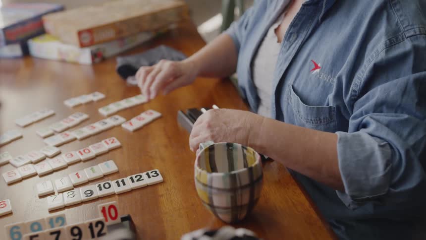 A boy places his game tiles on the table and his grandmother takes her turn