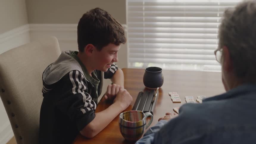 A boy and an older woman are playing a game at the kitchen table