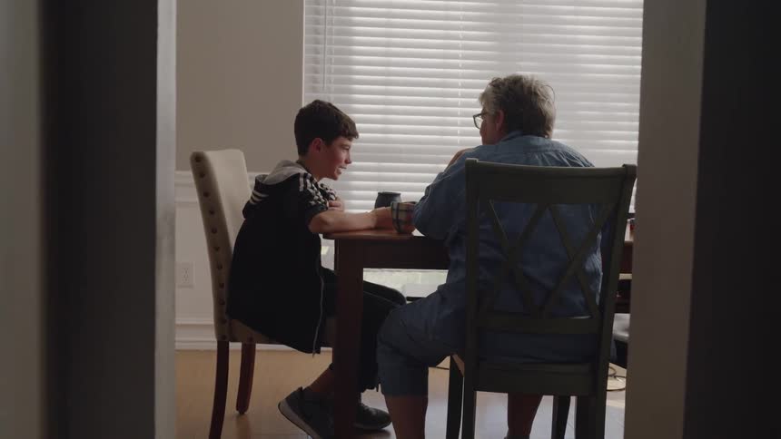 An elderly woman and boy talk at a dining room table