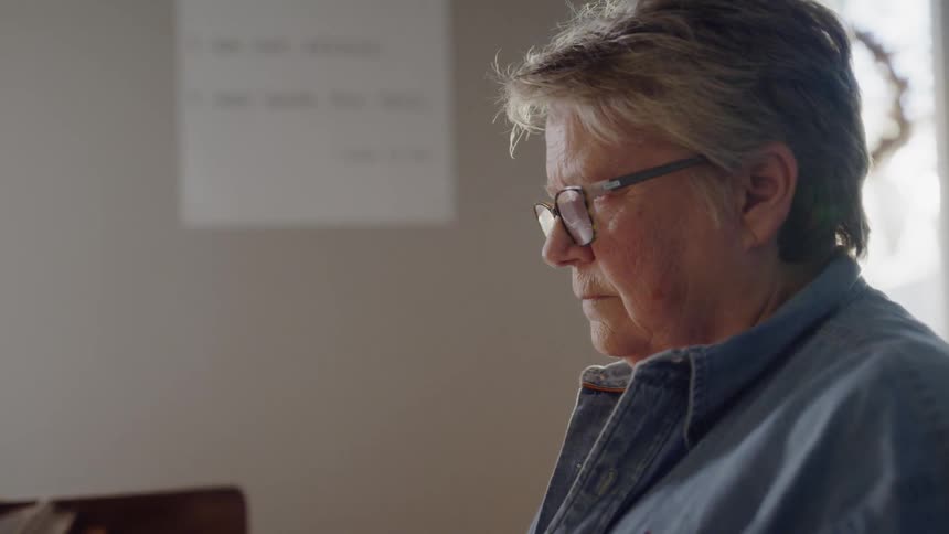 An older woman is playing a piano inside a room in daylight