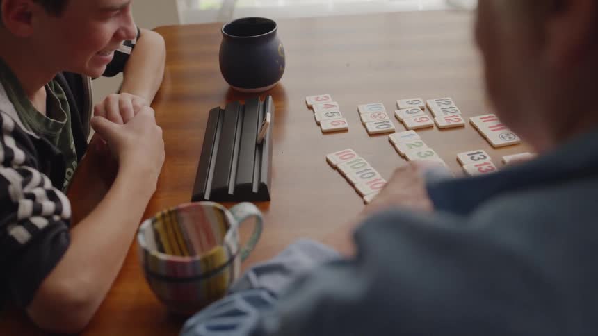 A boy plays a game with wooden tiles on the dining room table