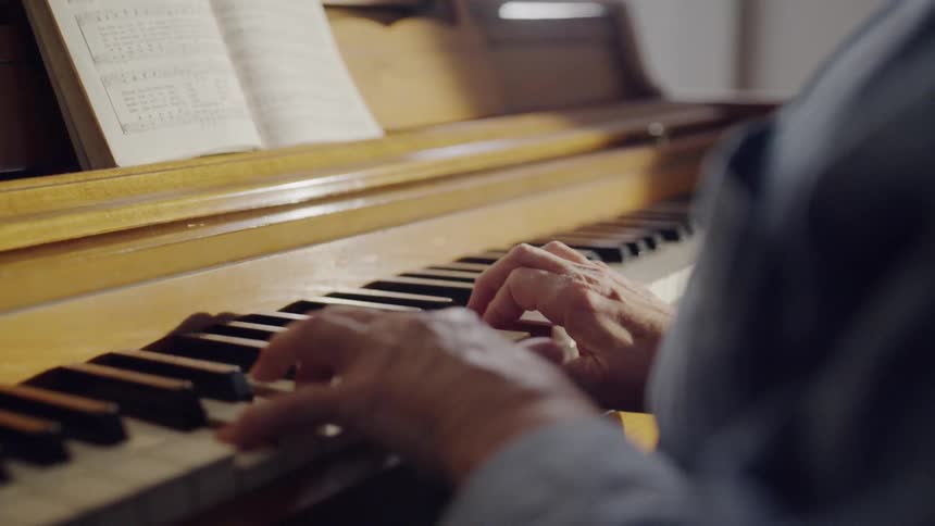 An older woman is playing a piano inside a room in daylight