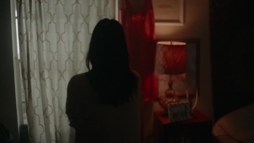 Woman stands next to a window with curtain over it