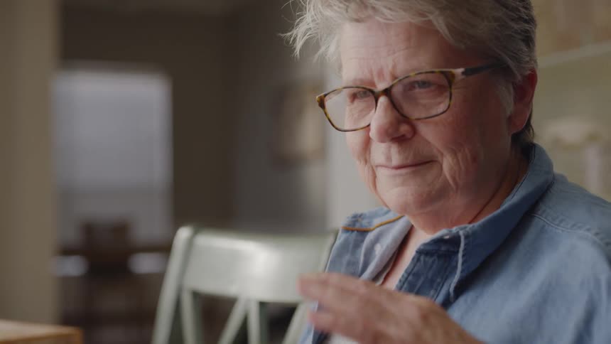 Elderly woman smiles, pushes her glasses up on her nose and talks to someone