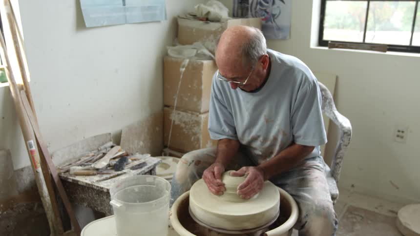 An elderly man forms a sculpture in a pottery wheel
