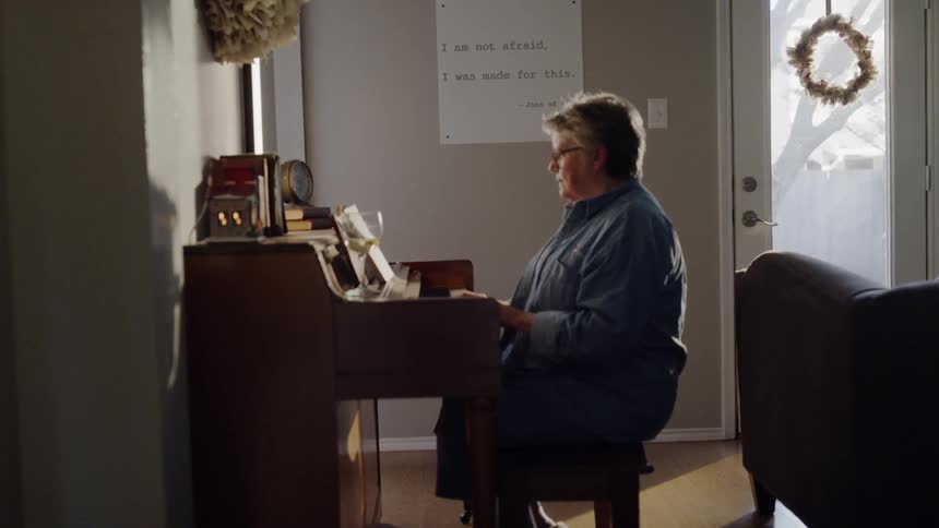 A woman is playing a piano her living room in daylight