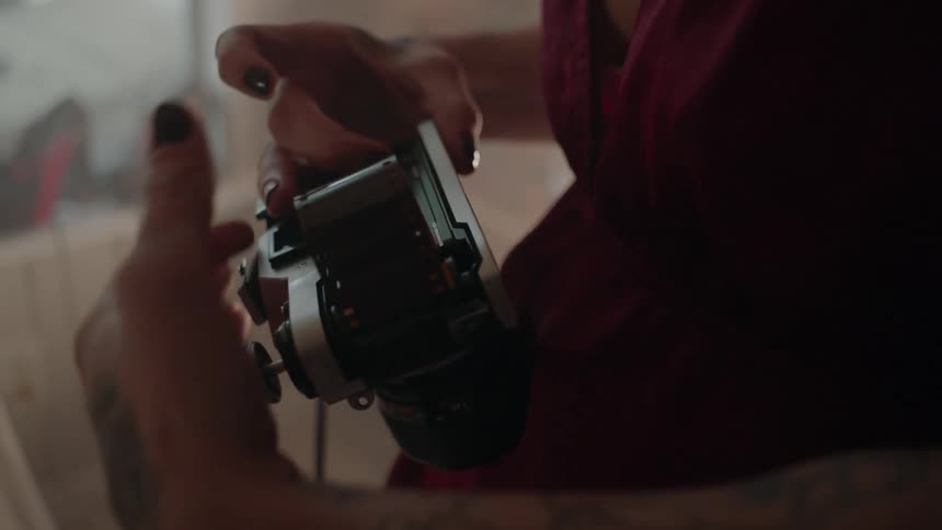 A woman is loading a 35mm camera with film as she stand inside in daylight