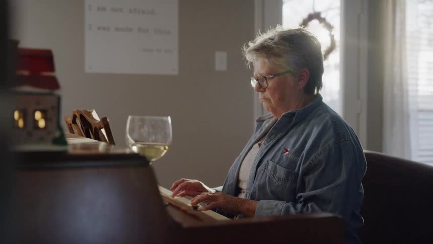 A woman wearing glasses plays the piano