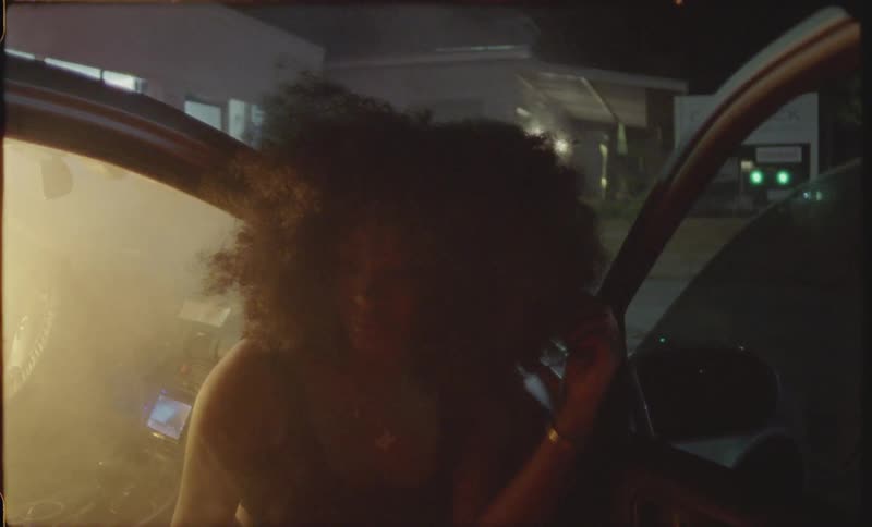 A woman is sitting on the edge of a car seat while the car is smoking