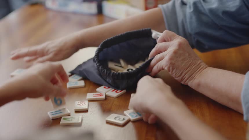 An older woman and a child are picking up scrabble-like tiles and mixing them