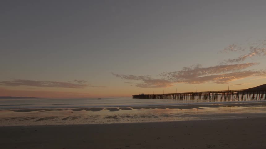 A pier goes out into the water of this beach at sunset