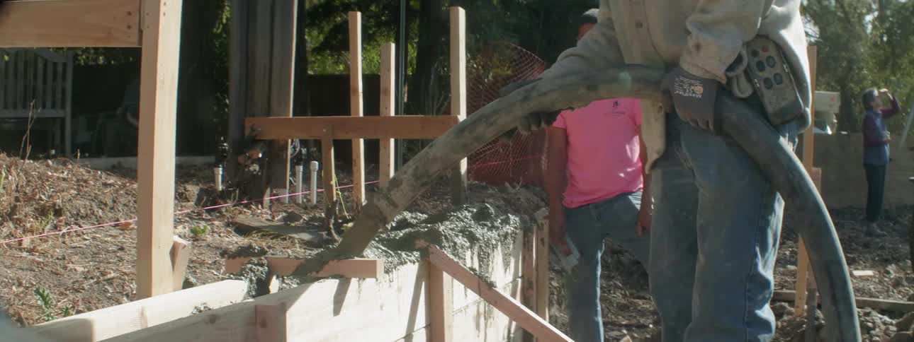 A landscaper is pouring cement from a hose