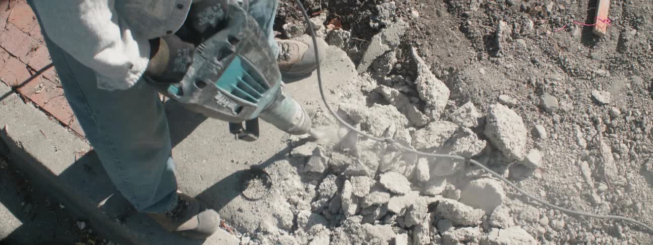 A worker is breaking up the cement with a jackhammer