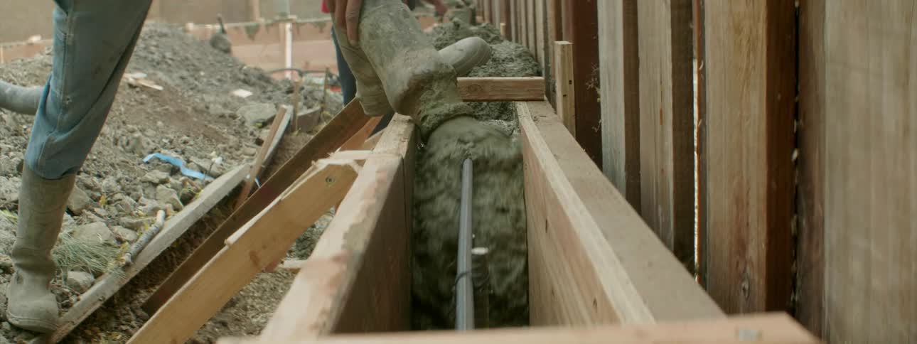 People are pouring concrete and shoveling it between boards