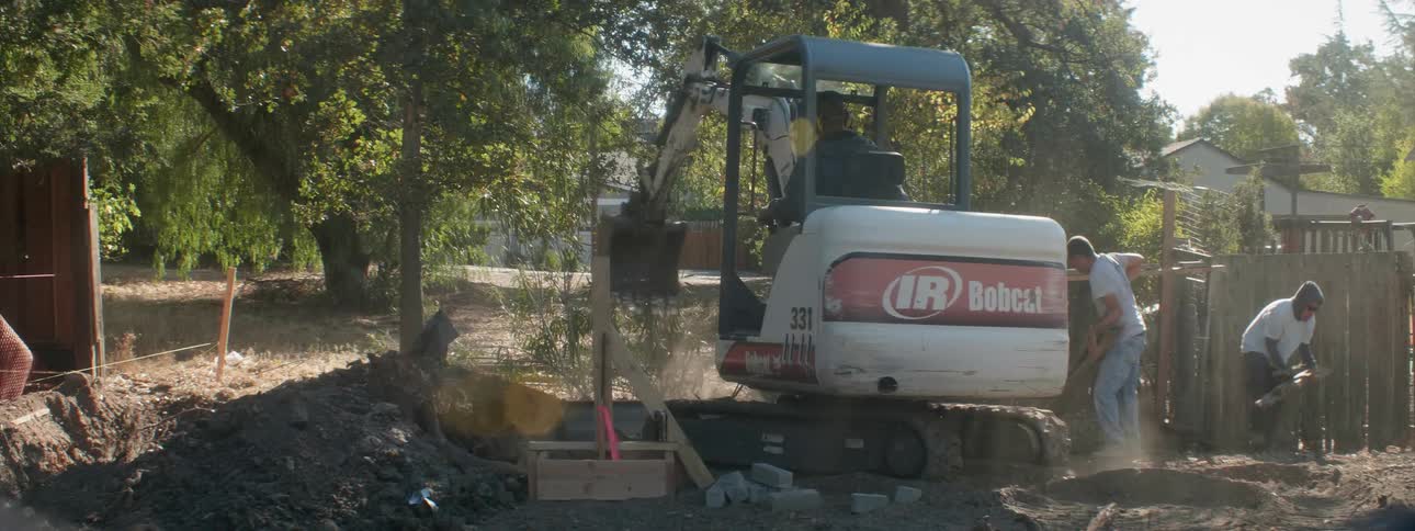 A man is operating a backhoe in a yard during the day