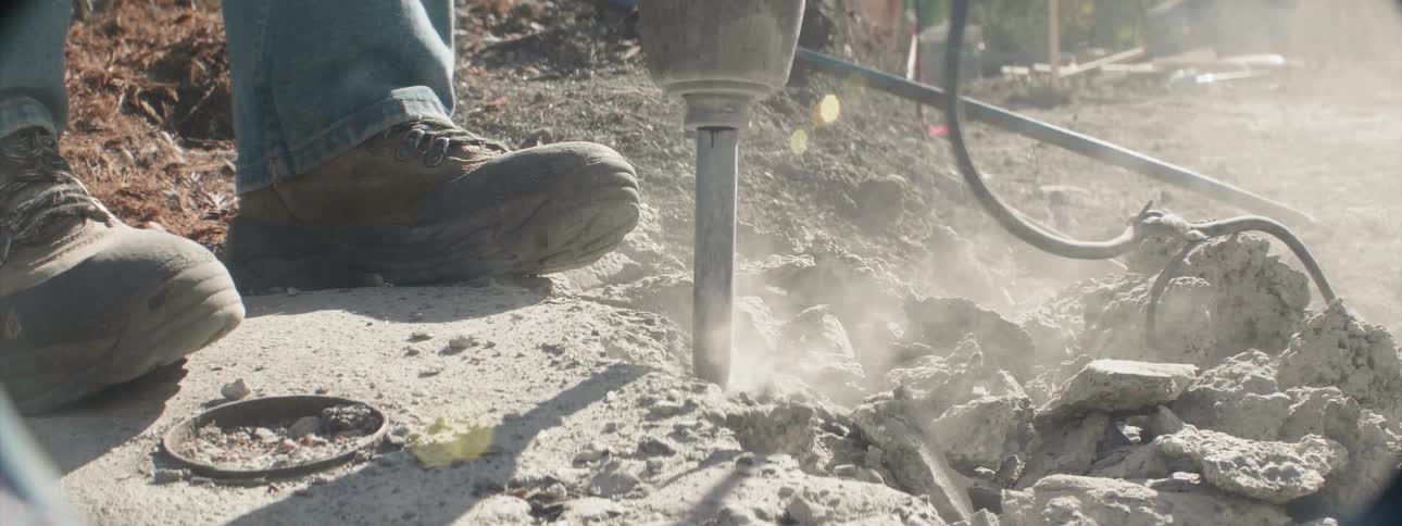 A worker is using a jackhammer to break up concrete during the day