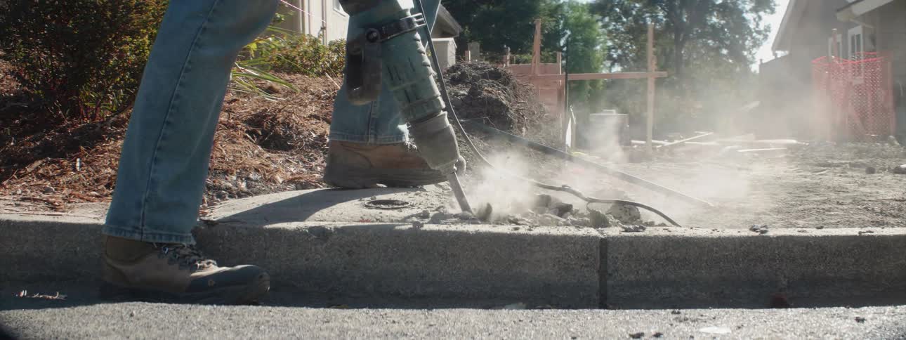 A construction worker uses a jackhammer on a job site
