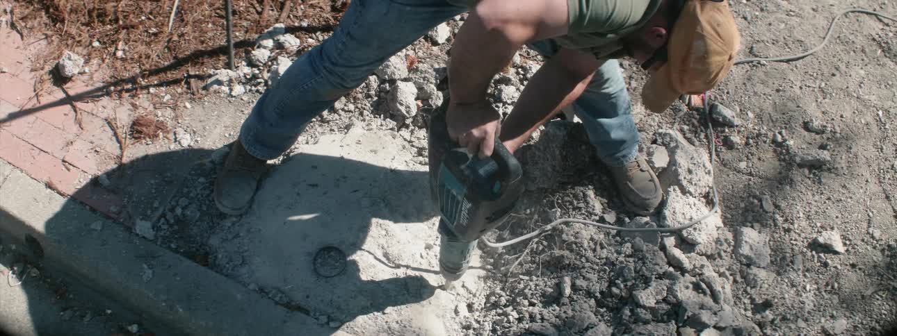 A worker is using a jackhammer to break up concrete during the day