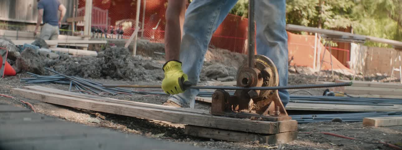 A construction worker is cutting a piece of rebar with a rebar cutter during the day