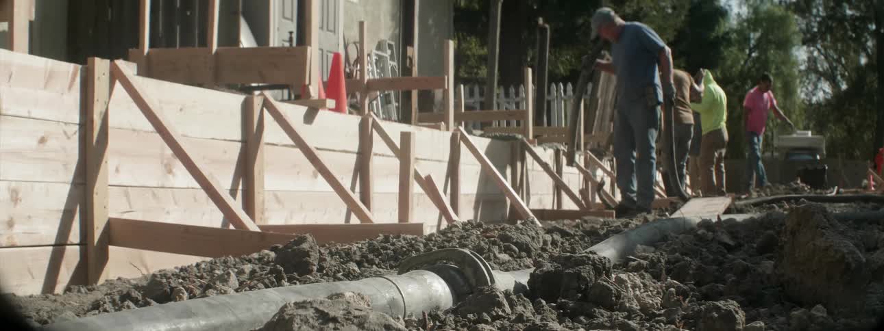 A worker uses a hose to fill a framed wall with cement