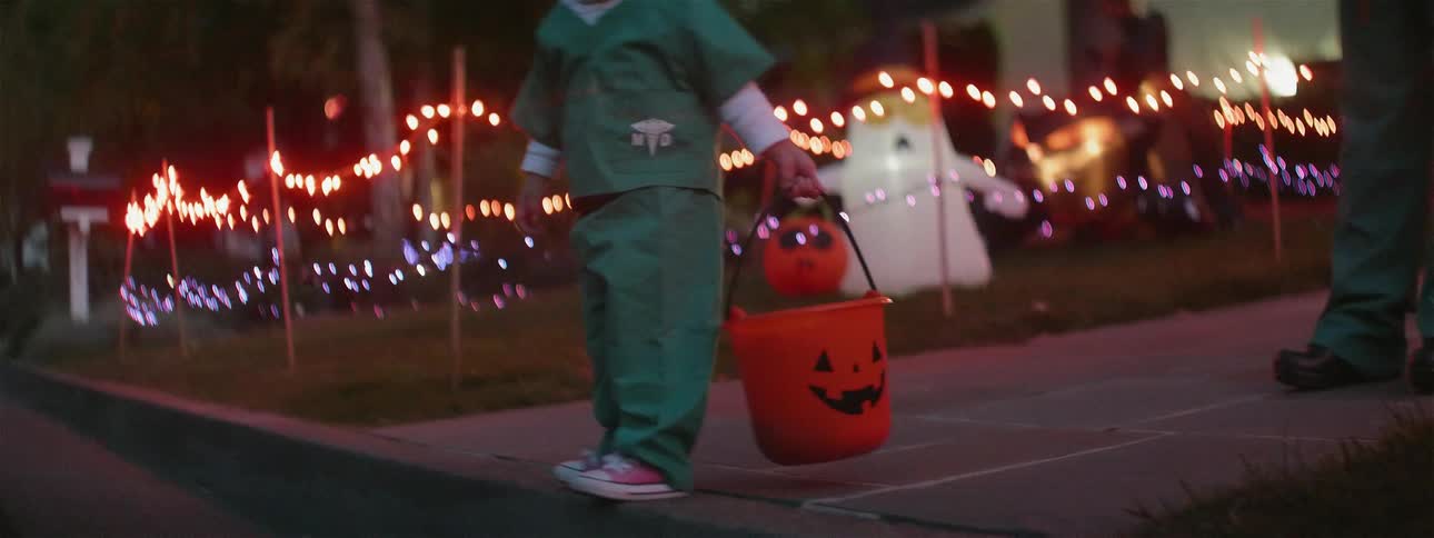 A young child is dressed as a doctor and is holding a orange pumpkin pail on halloween