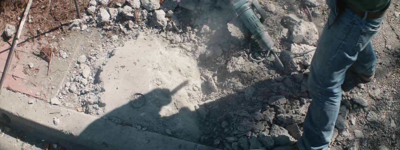A worker is breaking concrete with a sledgehammer