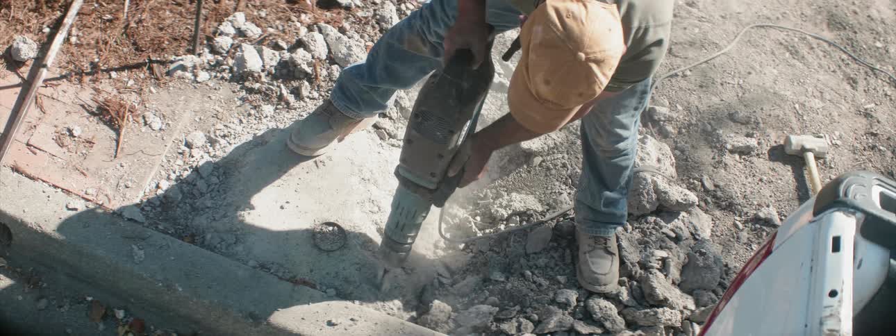 Man uses a jackhammer to drill into some concrete