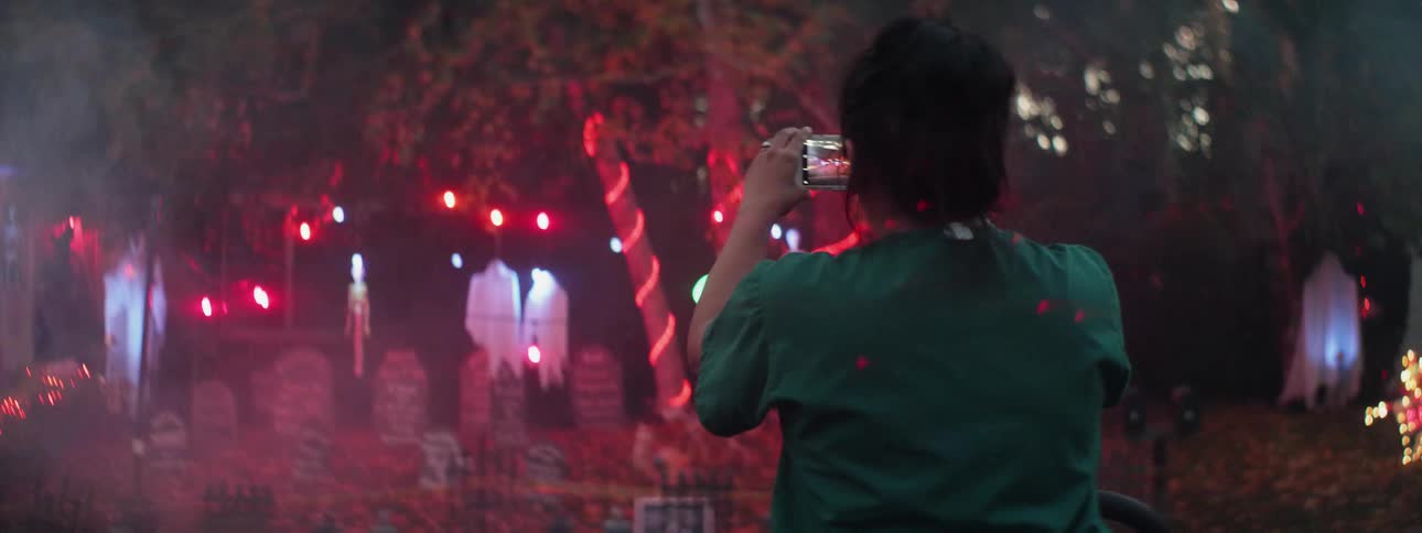 A woman photographs halloween decorations at night