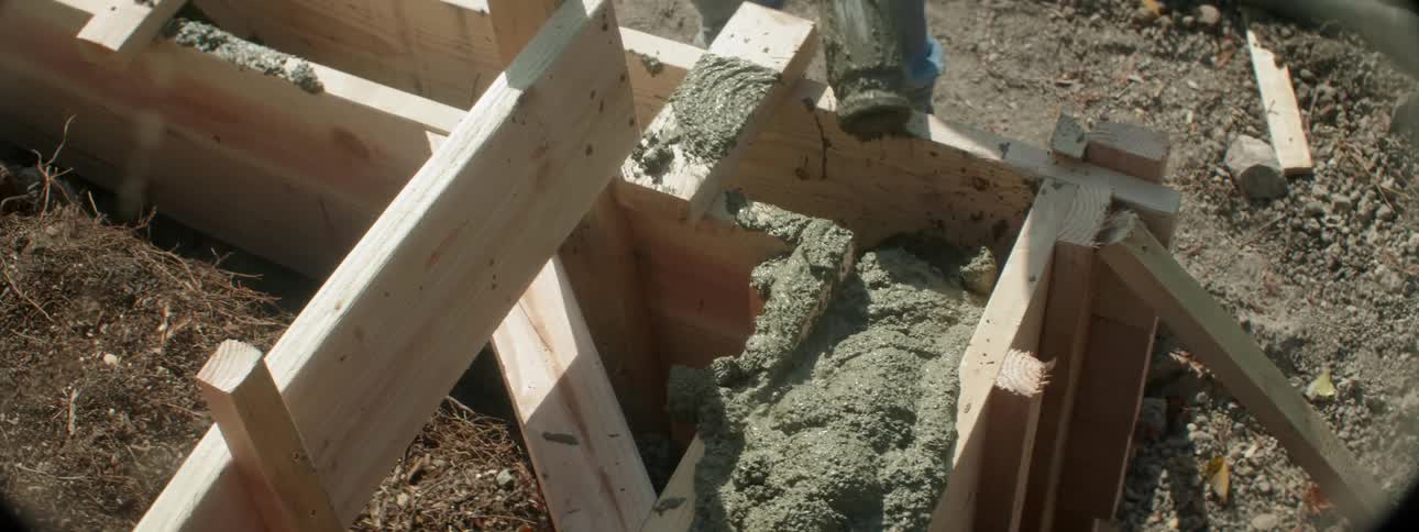 A person is pouring cement between the wooden boards