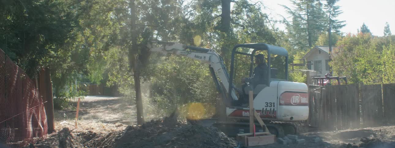 A man is using a construction vehicle to tear down a tree