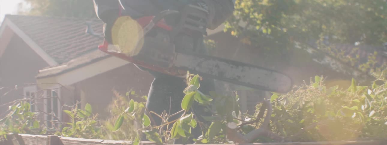 A landscaper in a truck bed uses a chainsaw to cut up branches