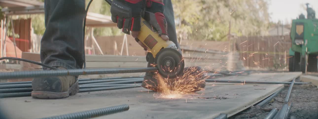 A worker is outside cutting a piece of rebar with a compact circular saw