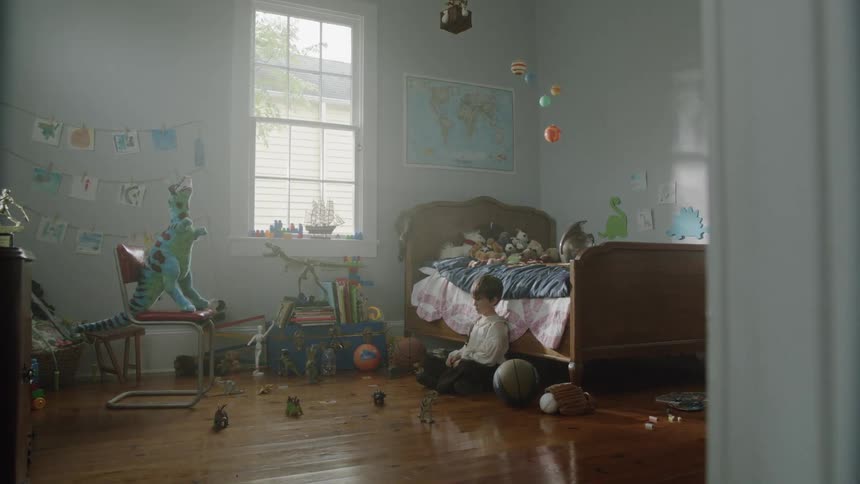 A child is sitting by the bed in the bedroom