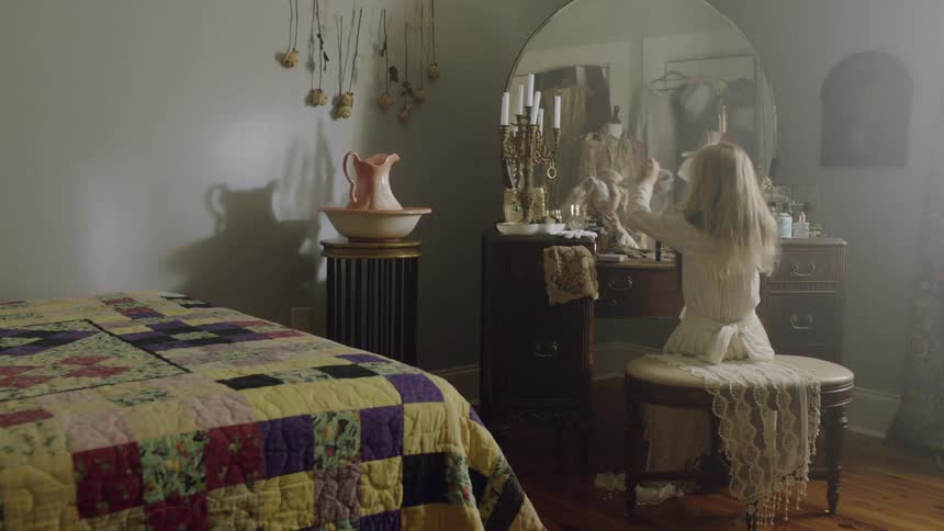 A young girl sits at a bedroom vanity