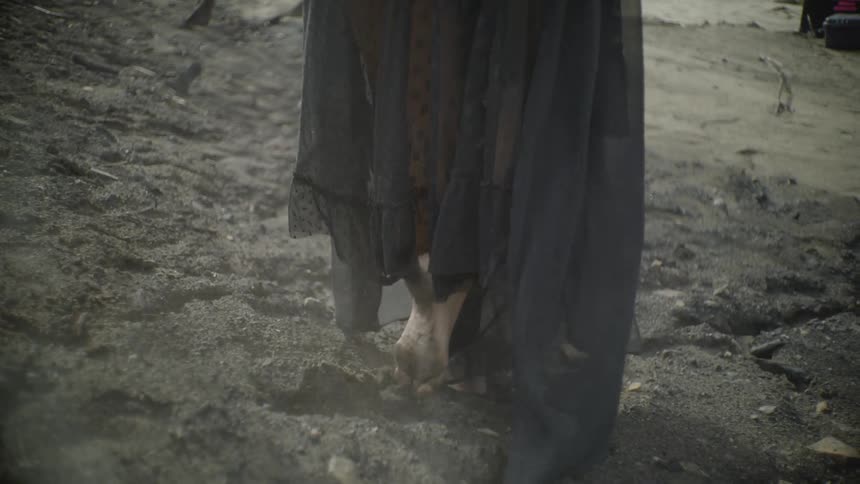 A person wearing a black dress wades through the mud