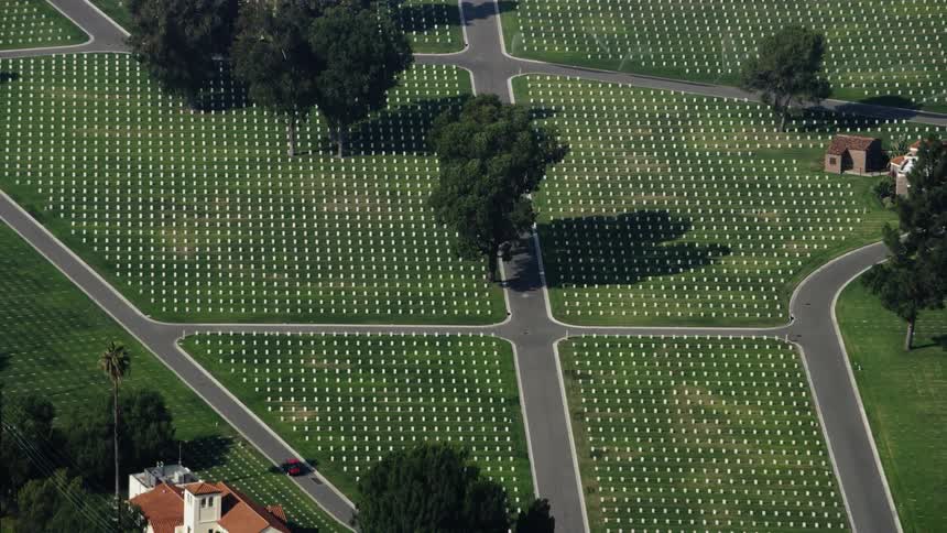 Trees are casting shadows across the headstones in a cemetery during the day