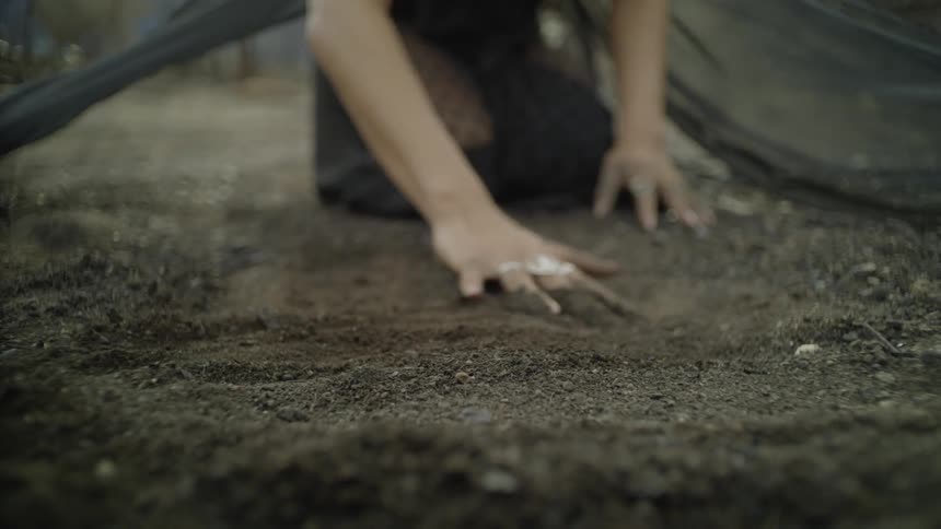 A woman kneels in dirt and rubs her hands on the ground