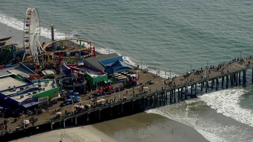 Many people walking on a large dock next to an amusement park