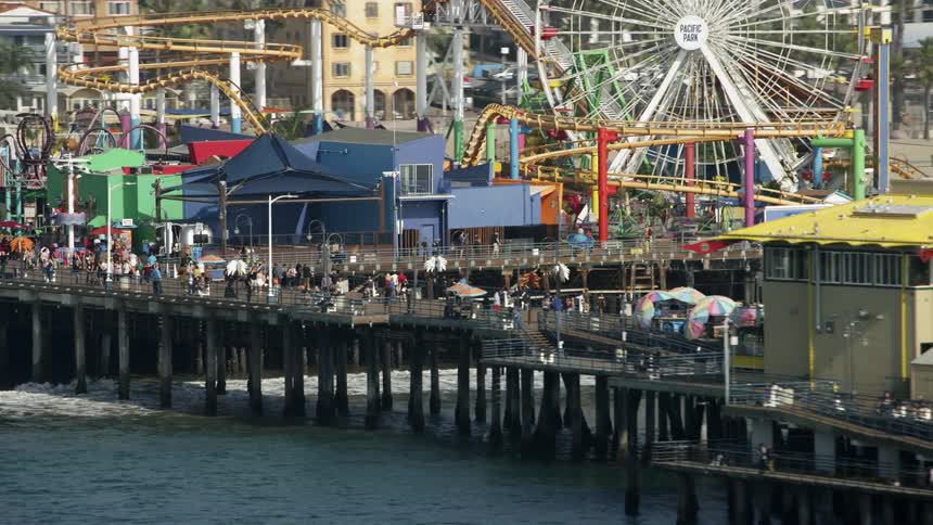 The amusement park is set up on the pier with many people walking