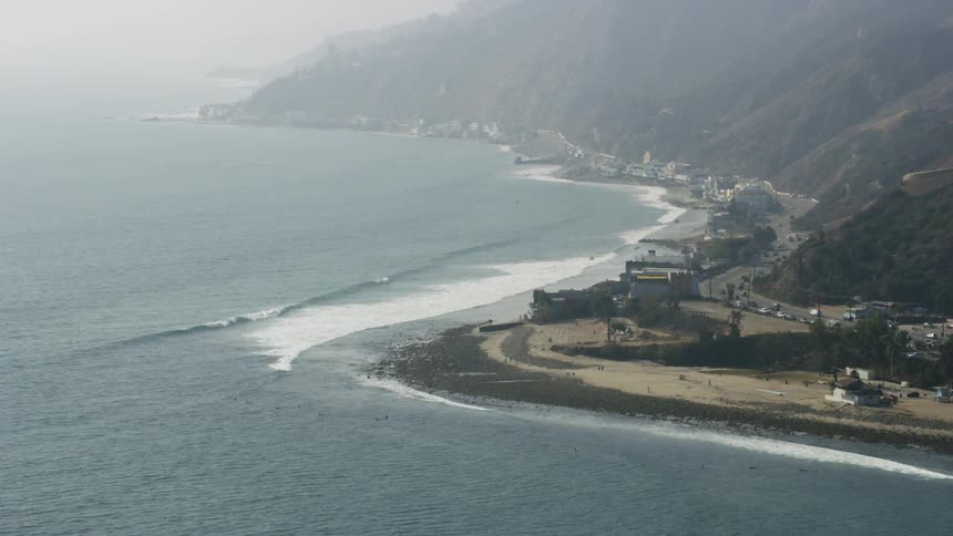 The waves slowly hit the shore as cars drive by on the nearby road