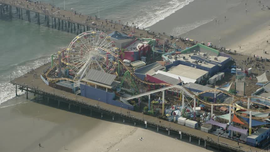 People walk on a pier near an amusement park at a beach on a sunny day