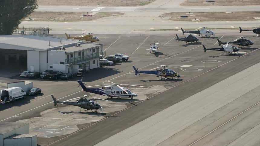 Helicopters are sitting outside a hangar at an airport during the day