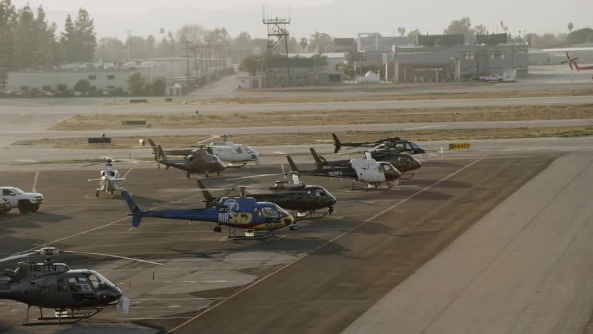 A group of helicopters are parked on the runaway on a cloudy day