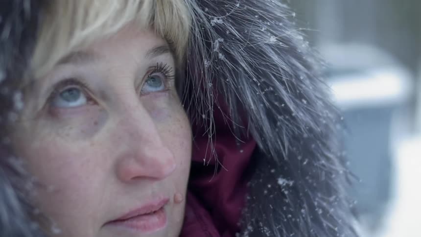 A woman is standing outside watching the snow as it falls during the day