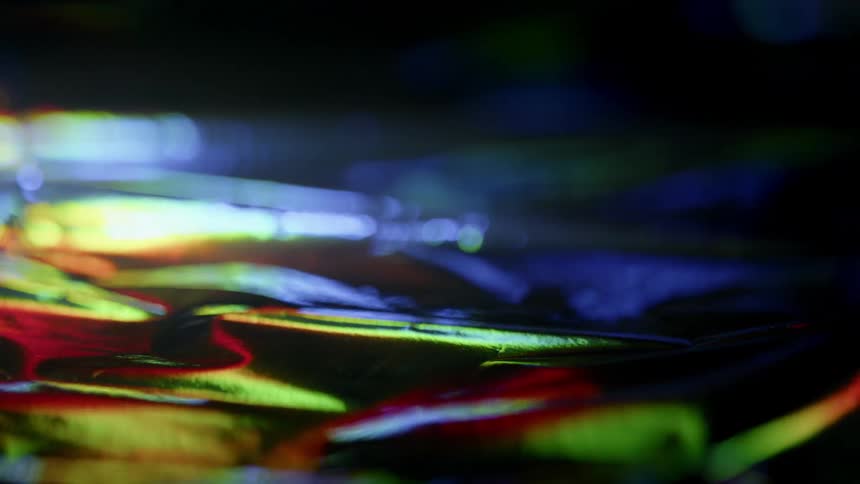 Light, color, and shadow are moving across a reflective surface
